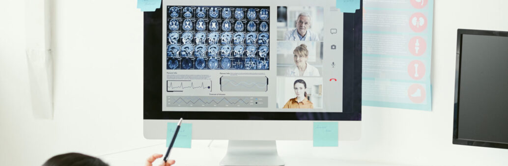Rear view of two doctors sitting at the table and examining the x-ray images on the computer together with their colleagues